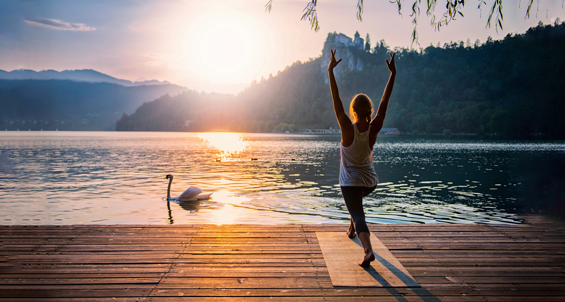 woman practicing yoga by the water at sunset